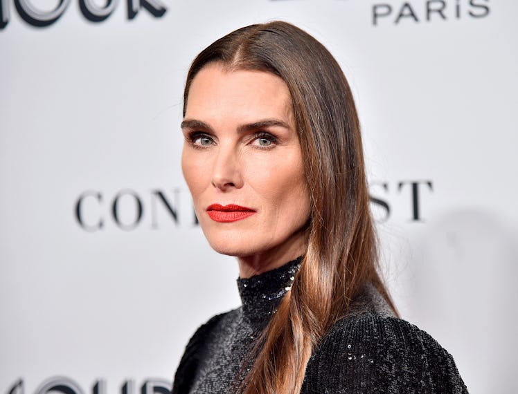Brooke Shields at a red carpet with straight hair, red lipstick and a shimmery black gown