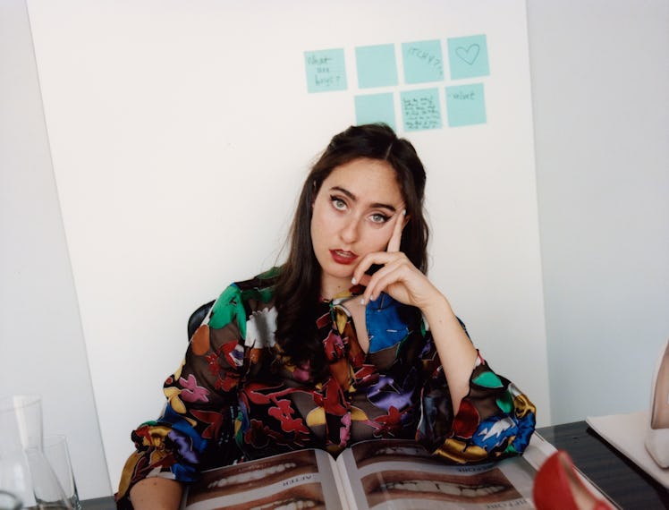 Catherine Cohen sitting at a table with a magazine spread out in front of her