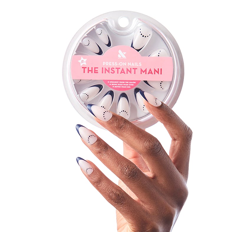 Hand wearing Olive & June's graphic, press-on nails while holding the packaging.