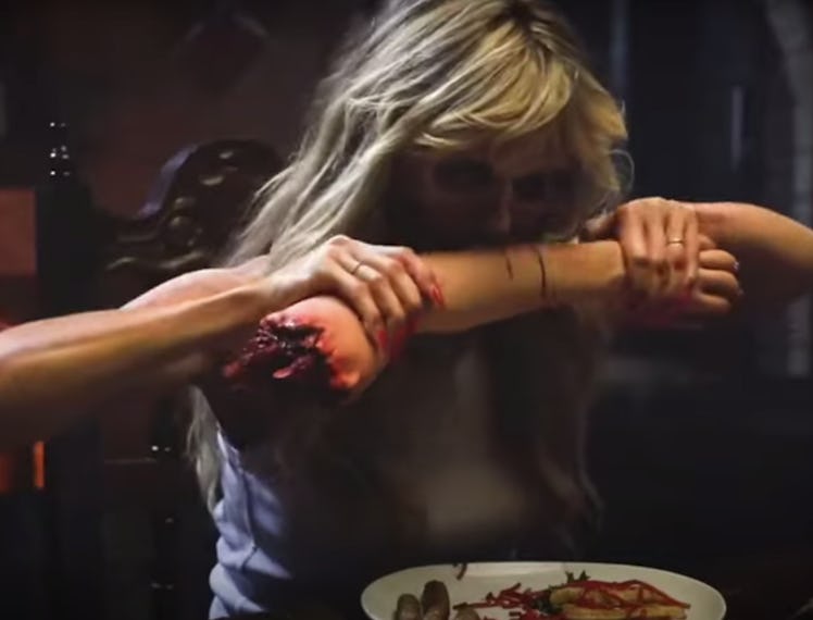 Heidi Klum biting into a cake that looks like a human arm in a short zombie film for Halloween