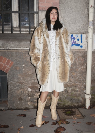 Showgoer at Paris Fashion Week wears fuzzy leopard coat, white dress, and cowboy boots.