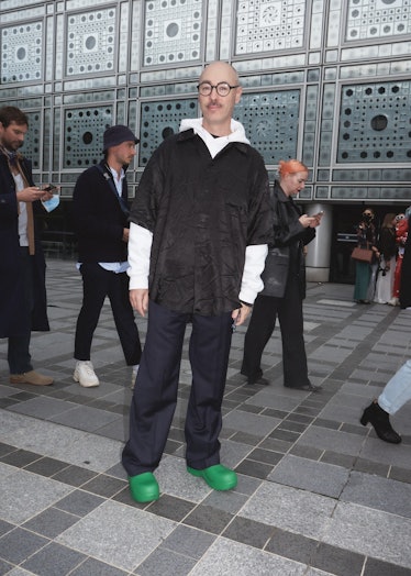 Showgoer at Paris Fashion Week wears black top over white hoodie with green rubber booties.