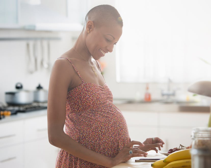 Pregnant woman in kitchen, smiling at tablet, building baby registry