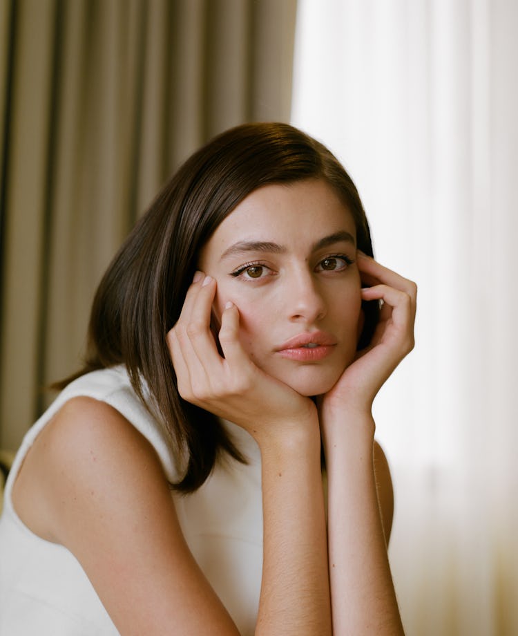 Diana Silvers posing for a picture in white dress keeping her hands under the chin and looking at th...