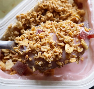 A spoonful of pink yogurt studded with granola bits.