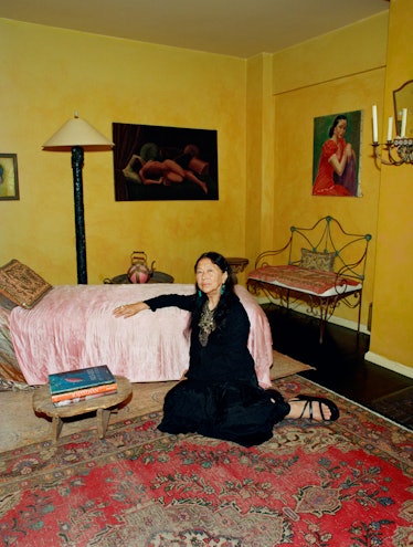 Nian fish, wearing an all-black outfit, reclines on the floor against a bed covered in a pink quilt.