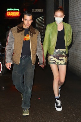 Sophie Turner wears camo print sequined skirt, black tank top, green leather jackets, and Louis Vuit...