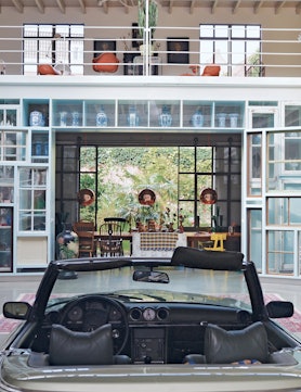 the atrium of a modern house in the netherlands, with a car parked in the center and art objects all...