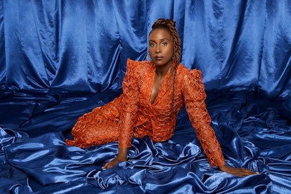 Issa Rae posing in an orange dress with a blue background