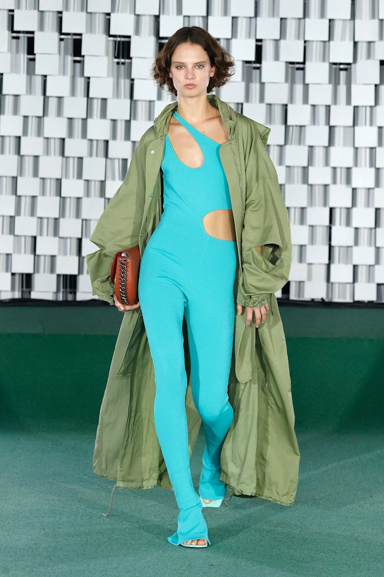 Model walks runway in teal body suit and green jacket from Stella McCartney spring 2022 collection.