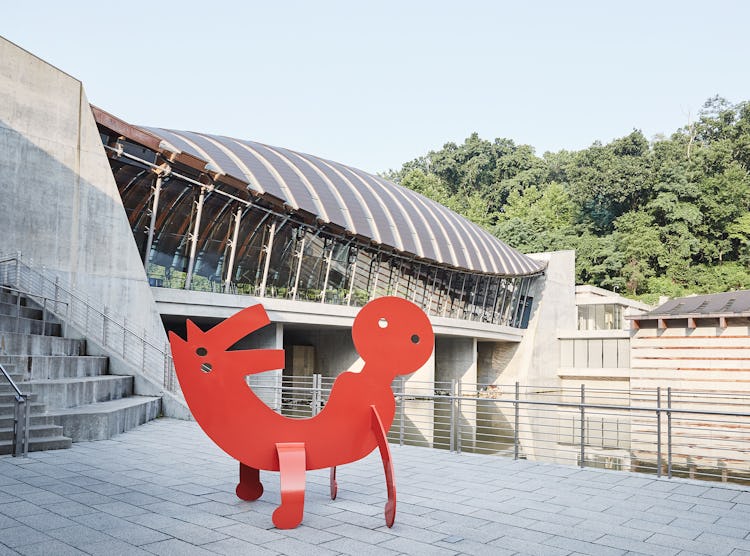 A red metal keith haring sculpture on a museum terrace