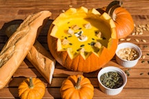 Table spread with a pumpkin with the top cut off, filled with soup