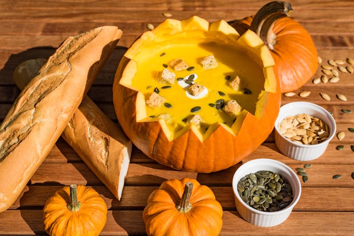 Table spread with a pumpkin with the top cut off, filled with soup