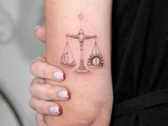 An image of a Libra Tattoo with a simple scale balancing a crescent moon and sun.