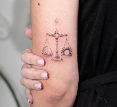 An image of a Libra Tattoo with a simple scale balancing a crescent moon and sun.