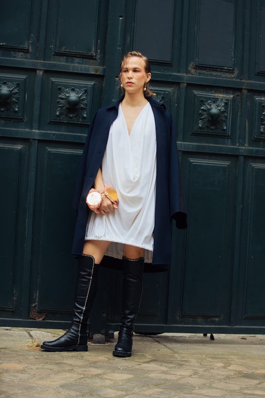 Tommy Dorfman wears a blue jacket with a white dress and knee-high black boots at the Loewe show on ...