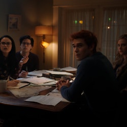 The core four of Riverdale sits at a table looking towards the camera in a scene from Riverdale Seas...