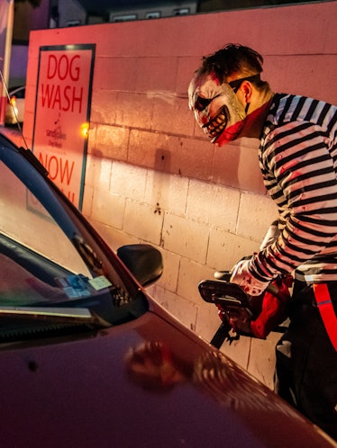 Two girls react as a character with a chain saw approaches their car at a drive-thru Halloween exper...
