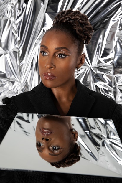 Issa Rae in a black Vera Wang jacket and Manluu jewelry gazing into the distance with a mirror below...