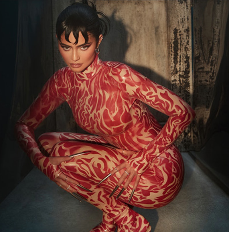 Kylie wearing a red swirly bodysuit and long silver talon nails and looking ominously at the camera