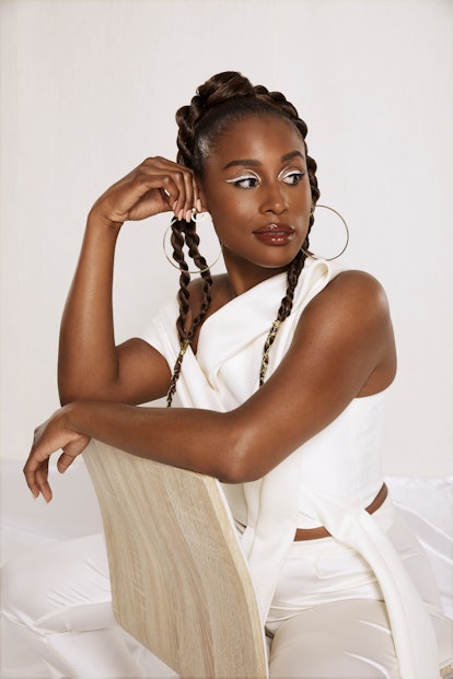 Issa Rae in a white Matthew Reisman pantsuit and and Sister Love hoop earrings sitting backwards on ...