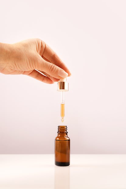 Hand holding glass dropper over serum bottle