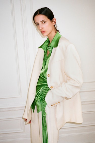 A model posing in a white Nanushka suit and a green satin shirt 