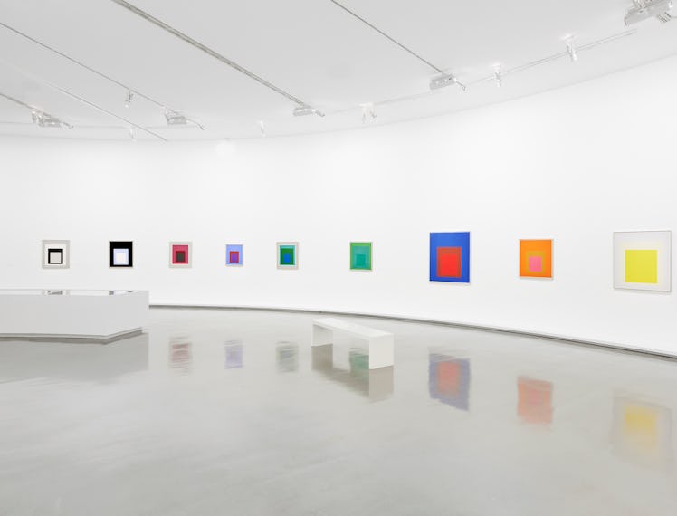 a row of colorful geometric paintings by josef albers in a white museum exhibition hall