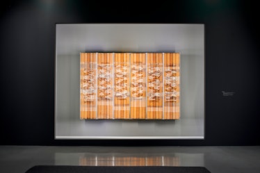 a brown and white woven wall hanging in a museum vitrine