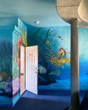 The entrance to a room that has walls painted entirely in an ocean theme with mermaids and other sea...