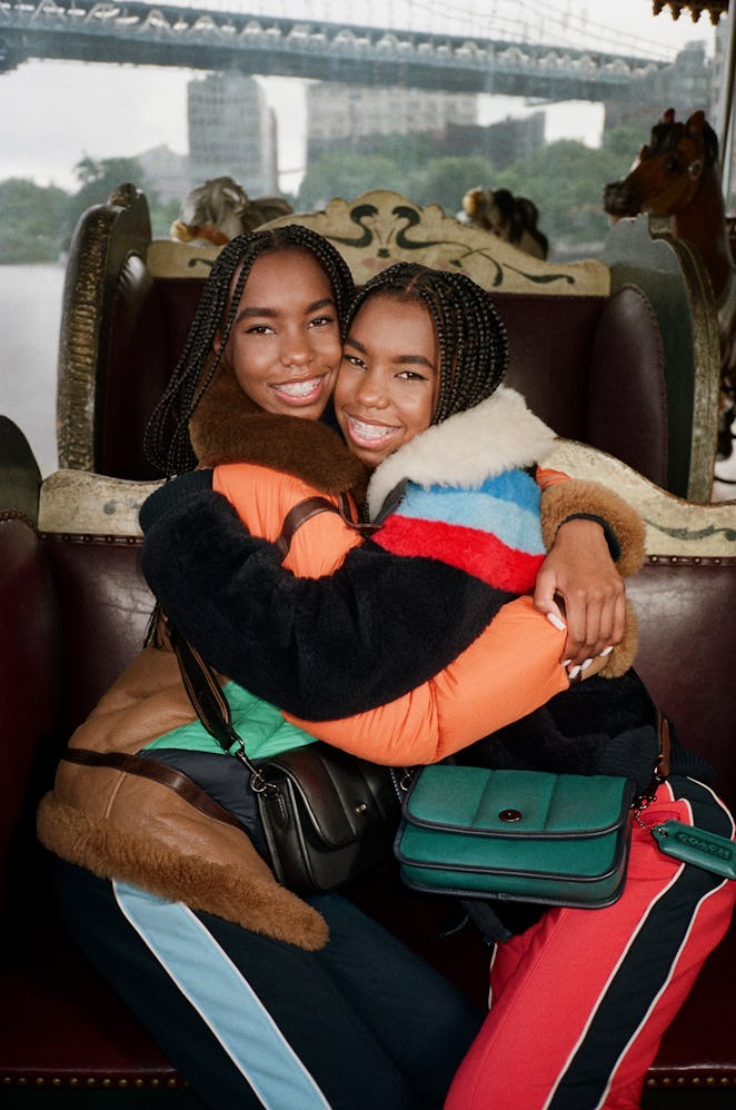 Two women hugging each other while wearing Coach's black and green small sized bags.