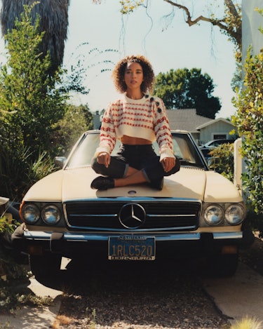 Alexandra Shipp from movie "Tick, tick... Boom!" sitting cross-legged on an old Mercedes