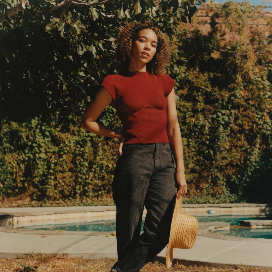 Alexandra Shipp from movie "Tick, tick... Boom!", in black jeans and maroon shirt holding a hat