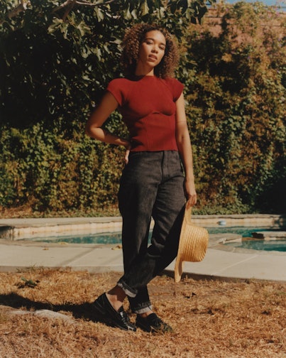 Alexandra Shipp from movie "Tick, tick... Boom!", in black jeans and maroon shirt holding a hat