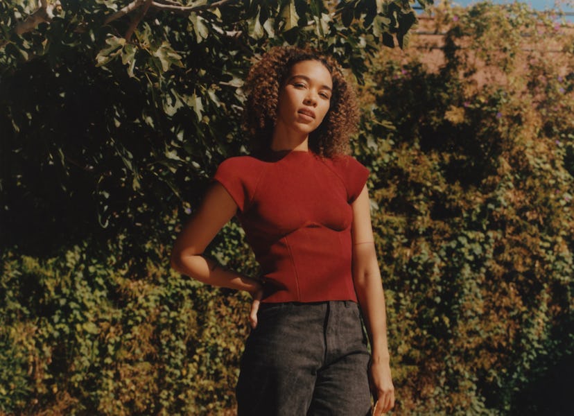 Alexandra Shipp from movie "Tick, tick... Boom!", in black jeans and maroon shirt holding a hat