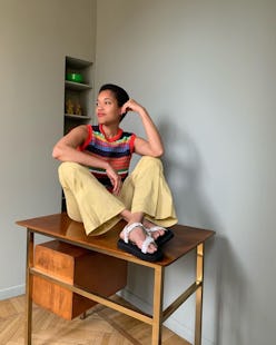 Tamu McPherson sitting on a table in yellow pants and a sweater vest.