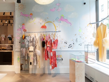 the inside of the Dauphinette Boutique in Rockefeller Center with muraled walls and clothes hanging ...