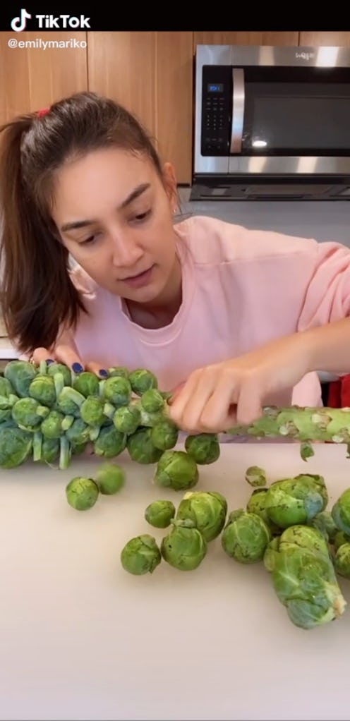 Screenshot of Emily Mariko hunching over countertop plucking brussels sprouts off a stalk.