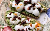 Close-up of two slices of toast spread with avocado, chunks of hard-boiled egg, and chili oil.