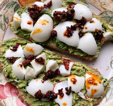 Close-up of two slices of toast spread with avocado, chunks of hard-boiled egg, and chili oil.