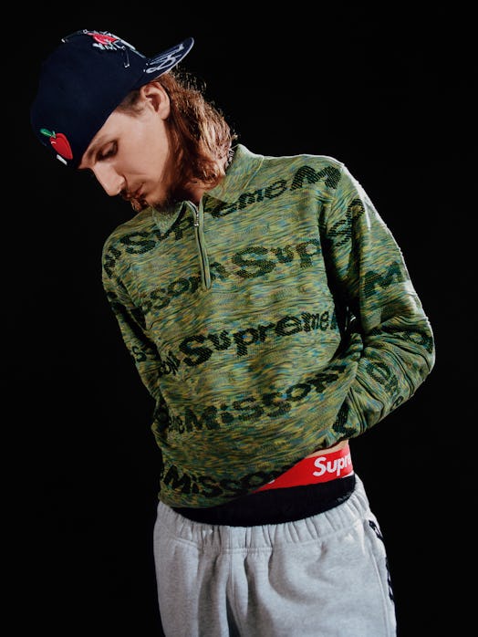 A model in a green Supreme branded quarter zip sweater