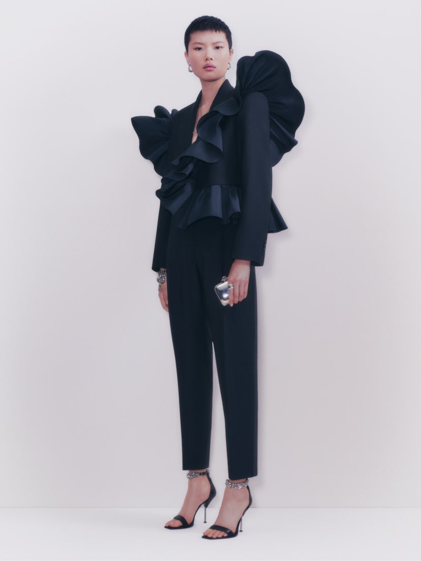 A model posing in a black suit with frills by Alexander McQueen