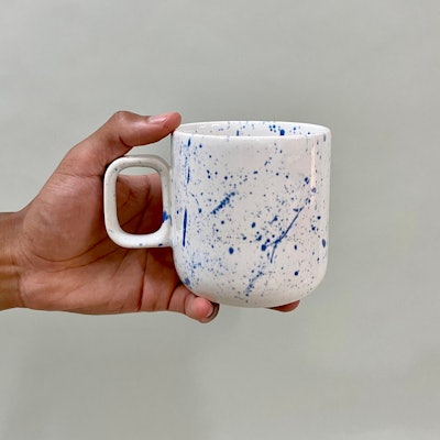 Hand holding a white mug with blue paint specks 