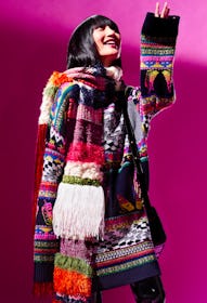 Model wears a colorful sweater and a knit scarf.