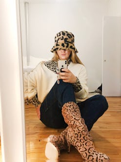 A woman taking a photo of herself in the mirror while sitting and wearing leopard inspired heel boot...