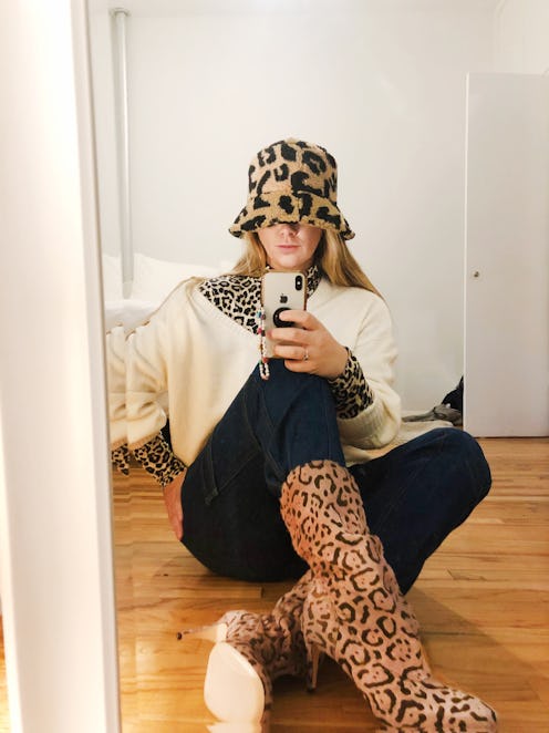 A woman taking a photo of herself in the mirror while sitting and wearing leopard inspired heel boot...