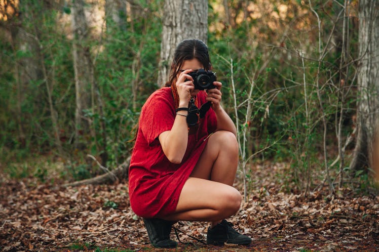 Young woman taking a picture in fall leaves, in need of November captions and quotes for Instagram.