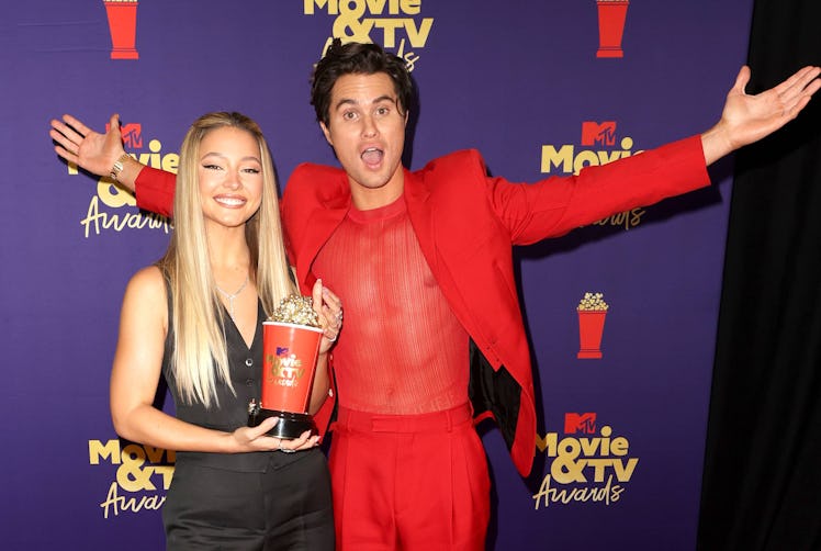 Chase Stokes in a red suit and shirt and Madelyn Cline in a black waistcoat and pants