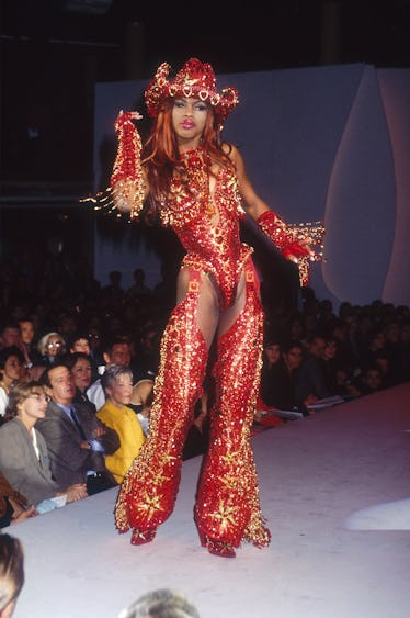 A fashion model wears a women's ready-to-wear glittery red cowgirl outfit with chaps and a cowboy ha...