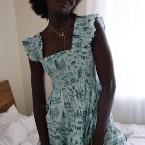 A woman wearing a printed green ruffle sleeve cotton dress while kneeling on a bed.